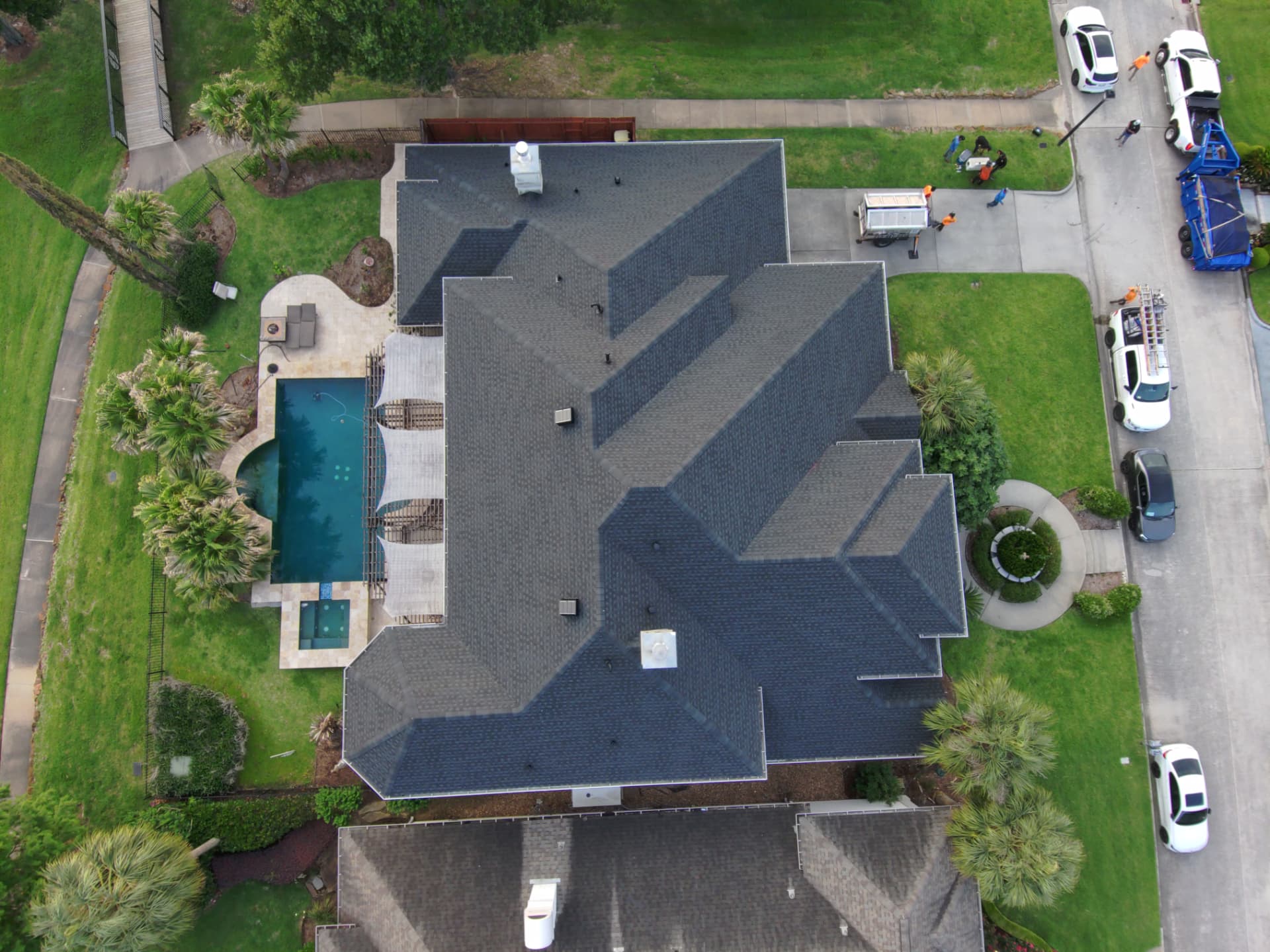 Overhead drone view of a completed shingle roof replacement on a two-story home with pool deck