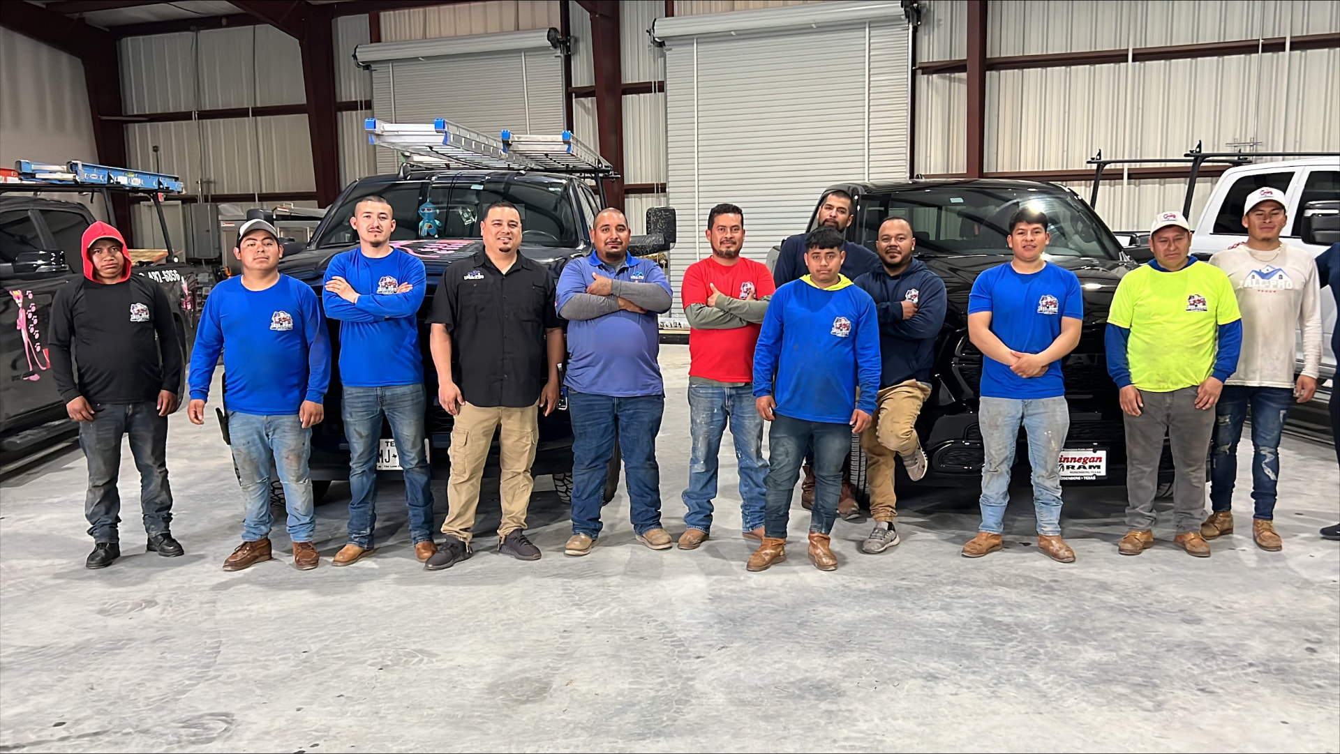 Full roofing crew standing together with company trucks and ladders at the Rosenberg, Texas shop