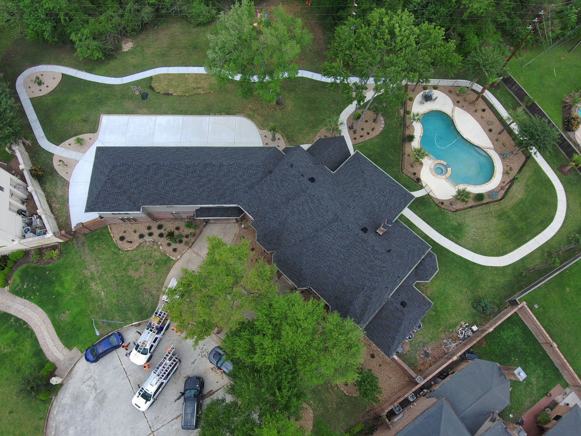 Overhead drone view of a finished charcoal shingle roof on an acreage home with pool and circular drive