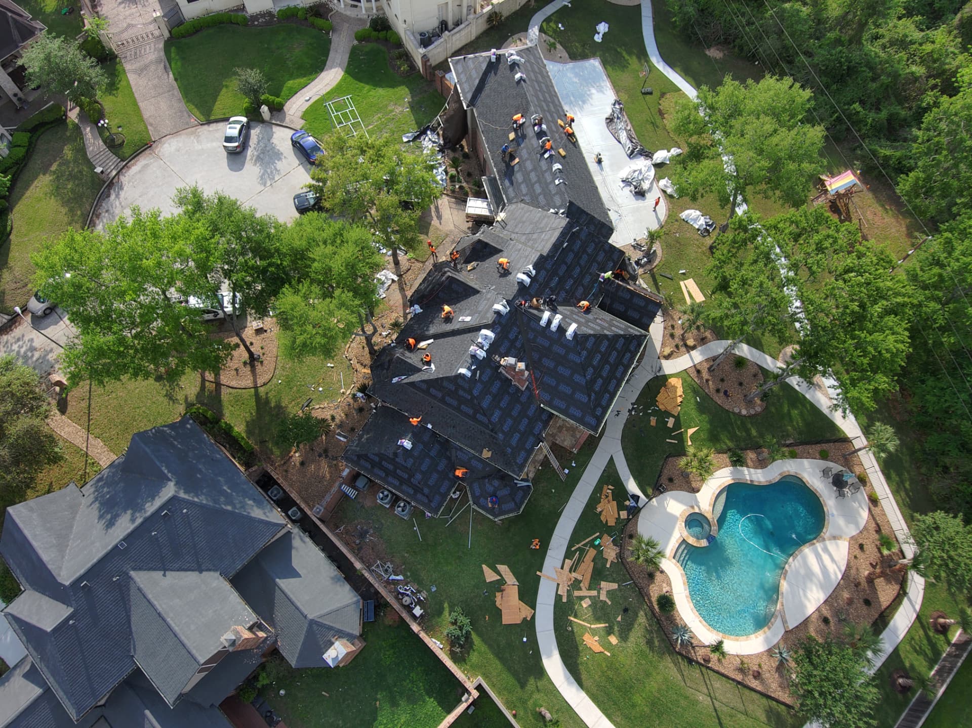 Aerial drone photo of a hip roof mid-replacement with crew and dumpster staged