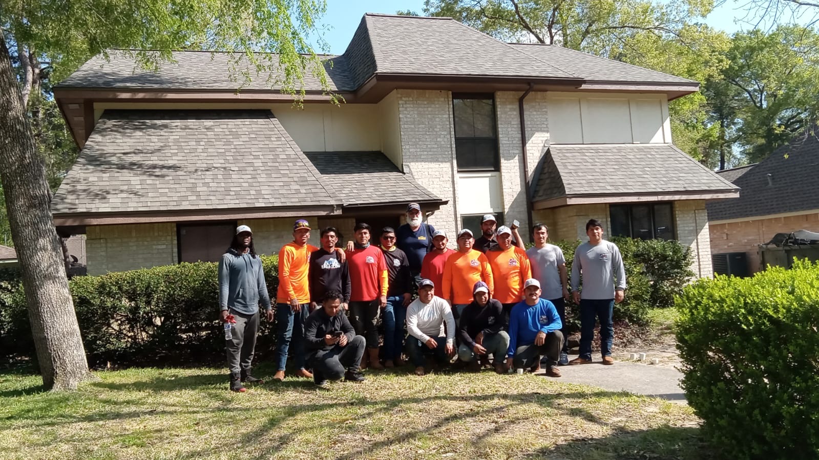 Roofing crew gathered in front of a completed two-story shingle roof replacement in the Houston area