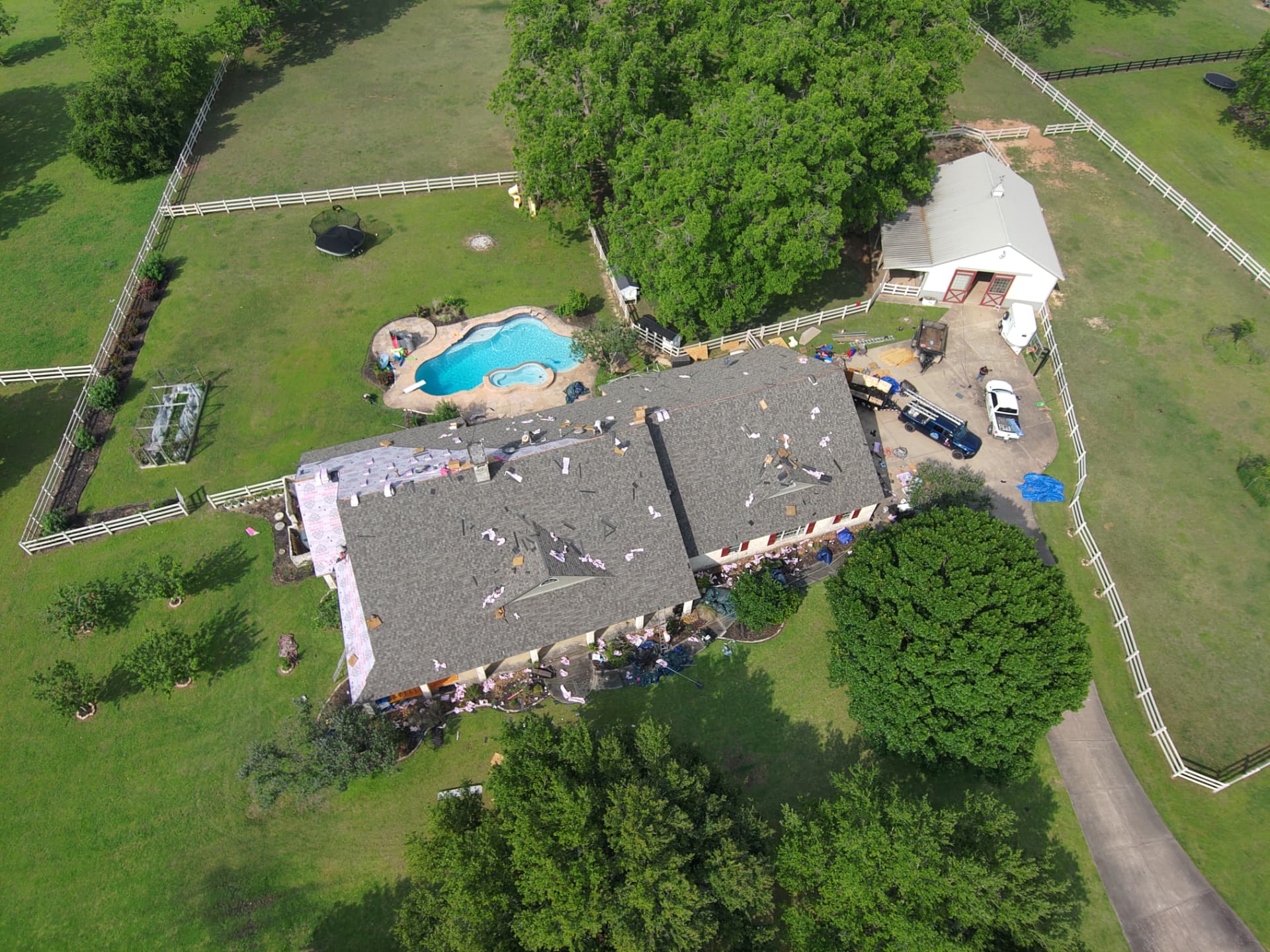 Aerial drone photo of a shingle roof replacement in progress on a country property with barn and pool