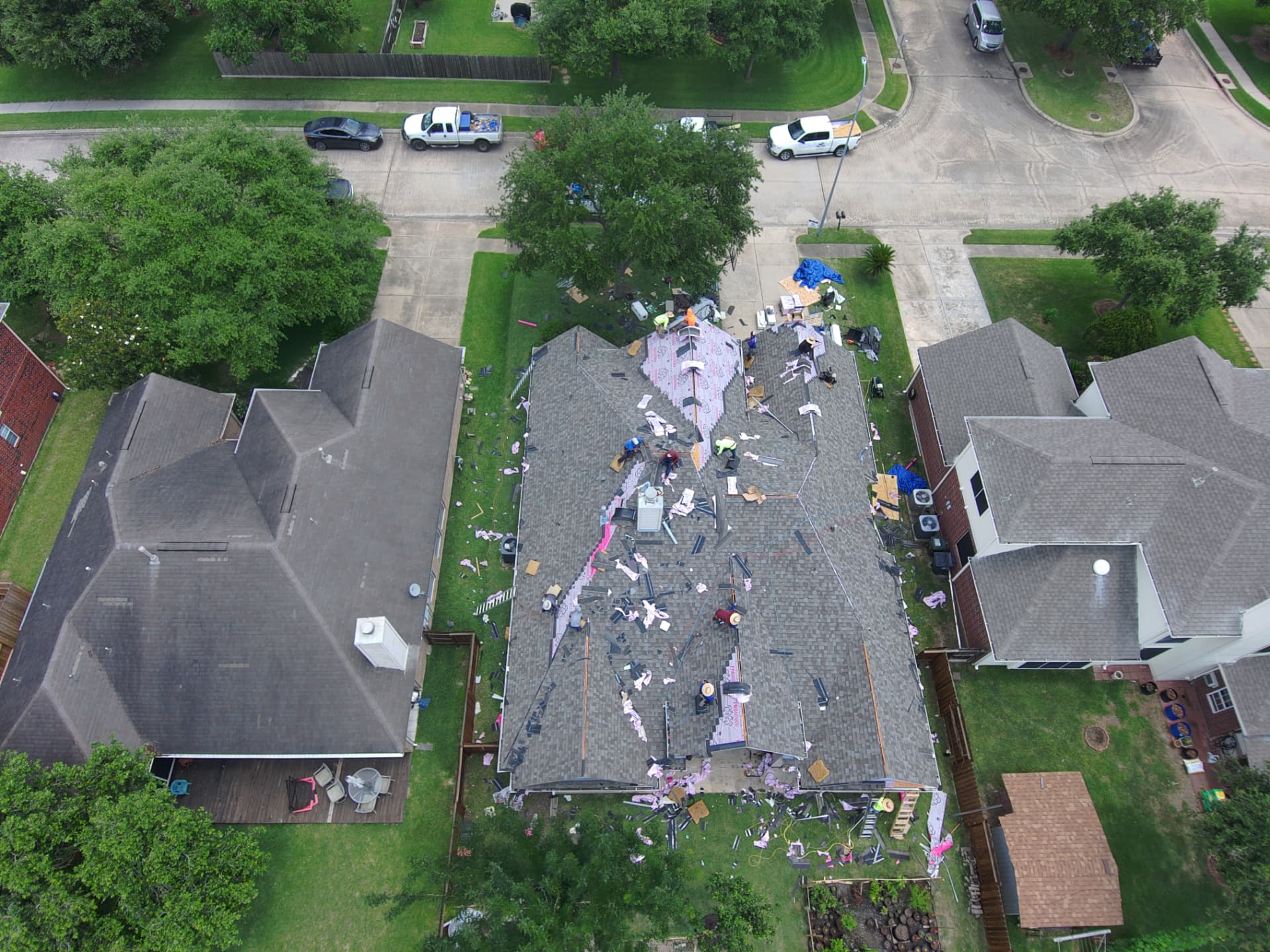 Top-down drone view of a roof tear-off and shingle replacement in a Houston-area neighborhood